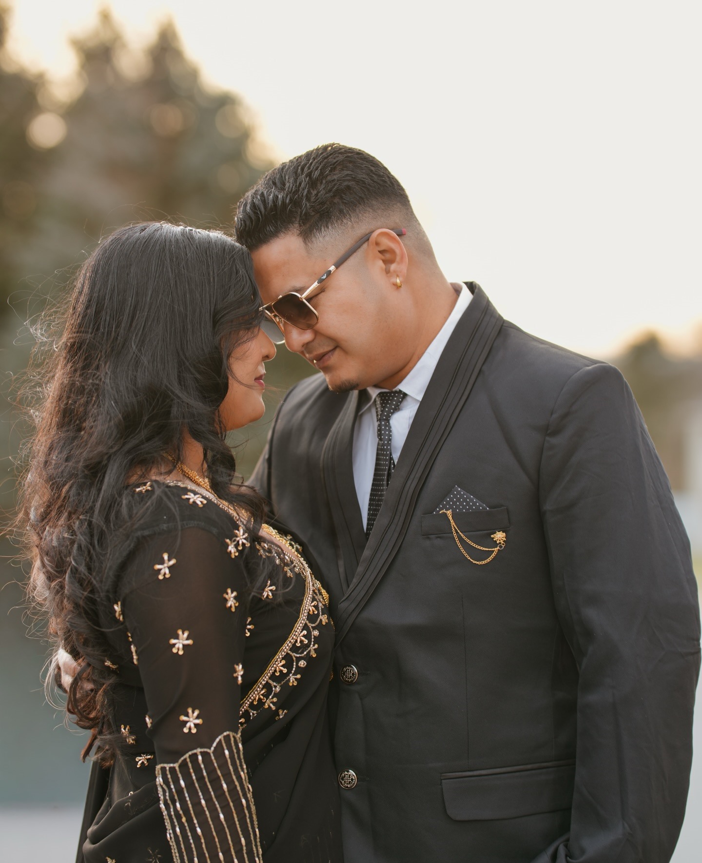A couple in black standing forehead to forehead in warm evening light
