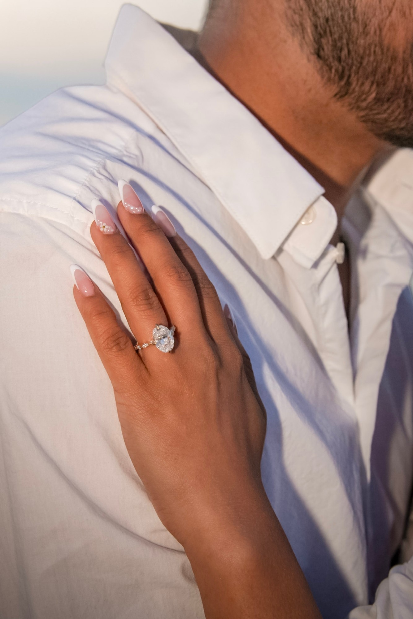 A hand wearing an oval engagement ring, resting on a white shirt