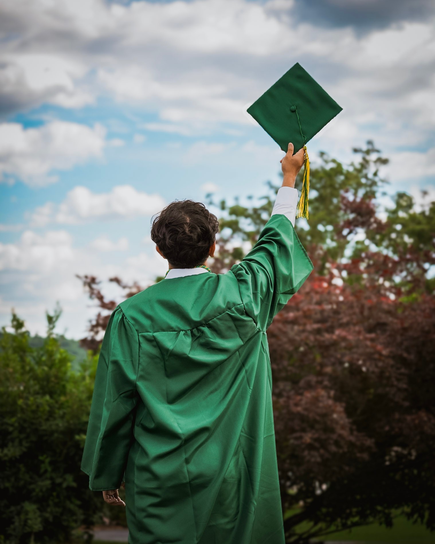 A graduate seen from behind, raising a green cap to the sky